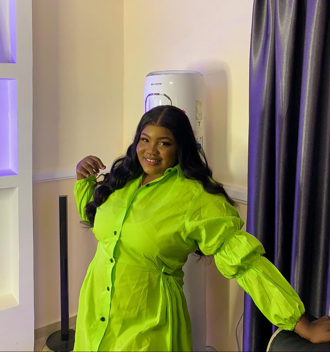 Woman in a bright green dress standing indoors next to a curtain